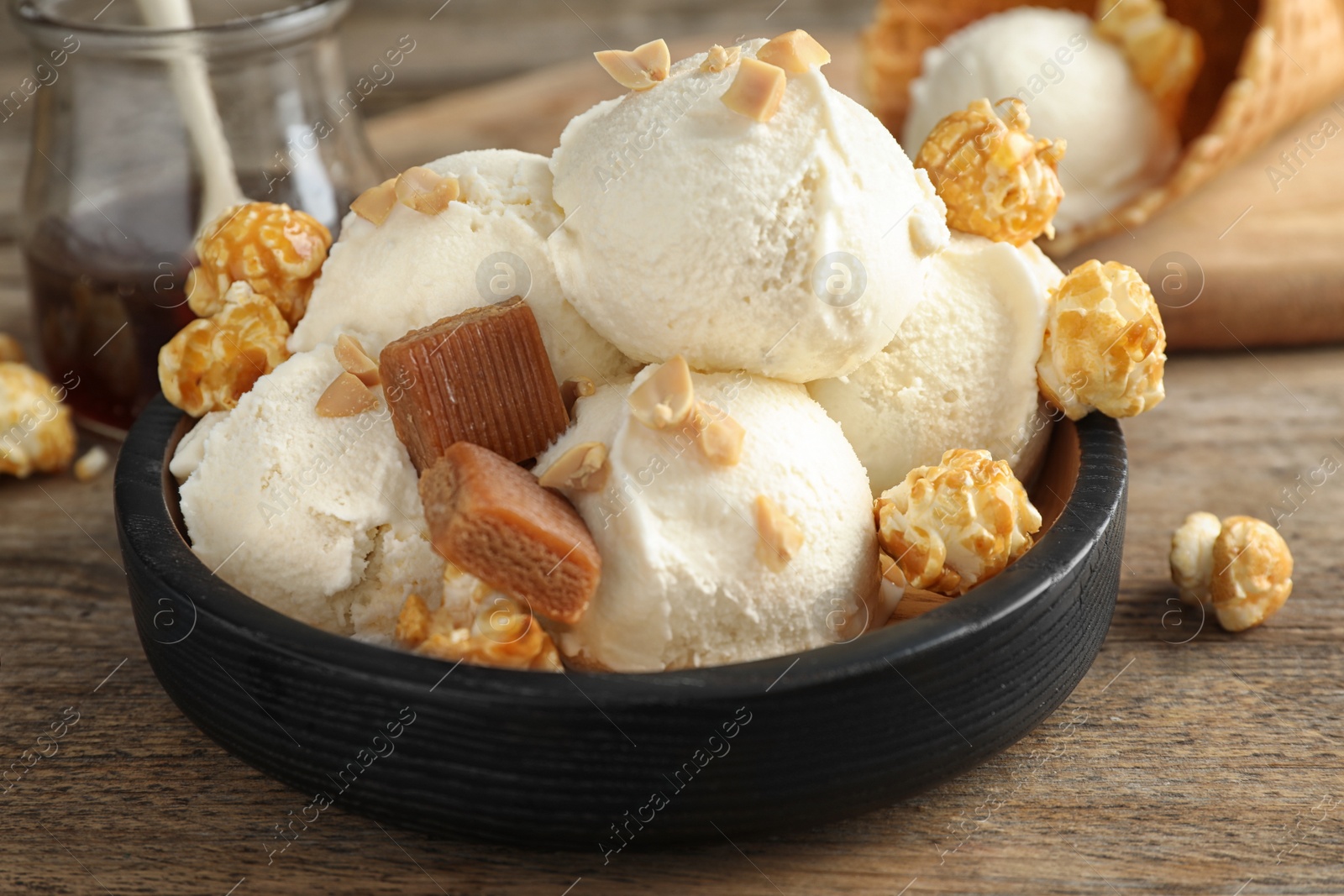 Photo of Plate of delicious ice cream with caramel candies and popcorn on wooden table, closeup