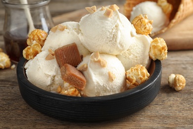 Photo of Plate of delicious ice cream with caramel candies and popcorn on wooden table, closeup