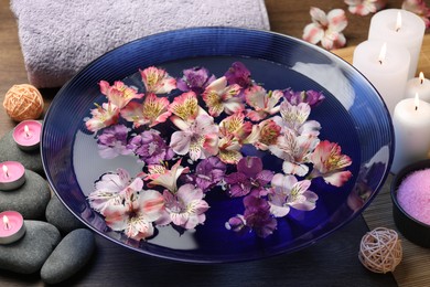 Photo of Bowl of water with flowers, candles, stones and towel on wooden table. Spa treatment