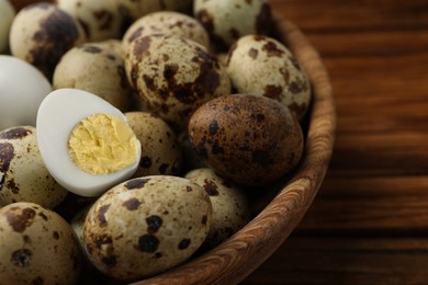 Unpeeled and peeled hard boiled quail eggs in bowl on wooden table, closeup