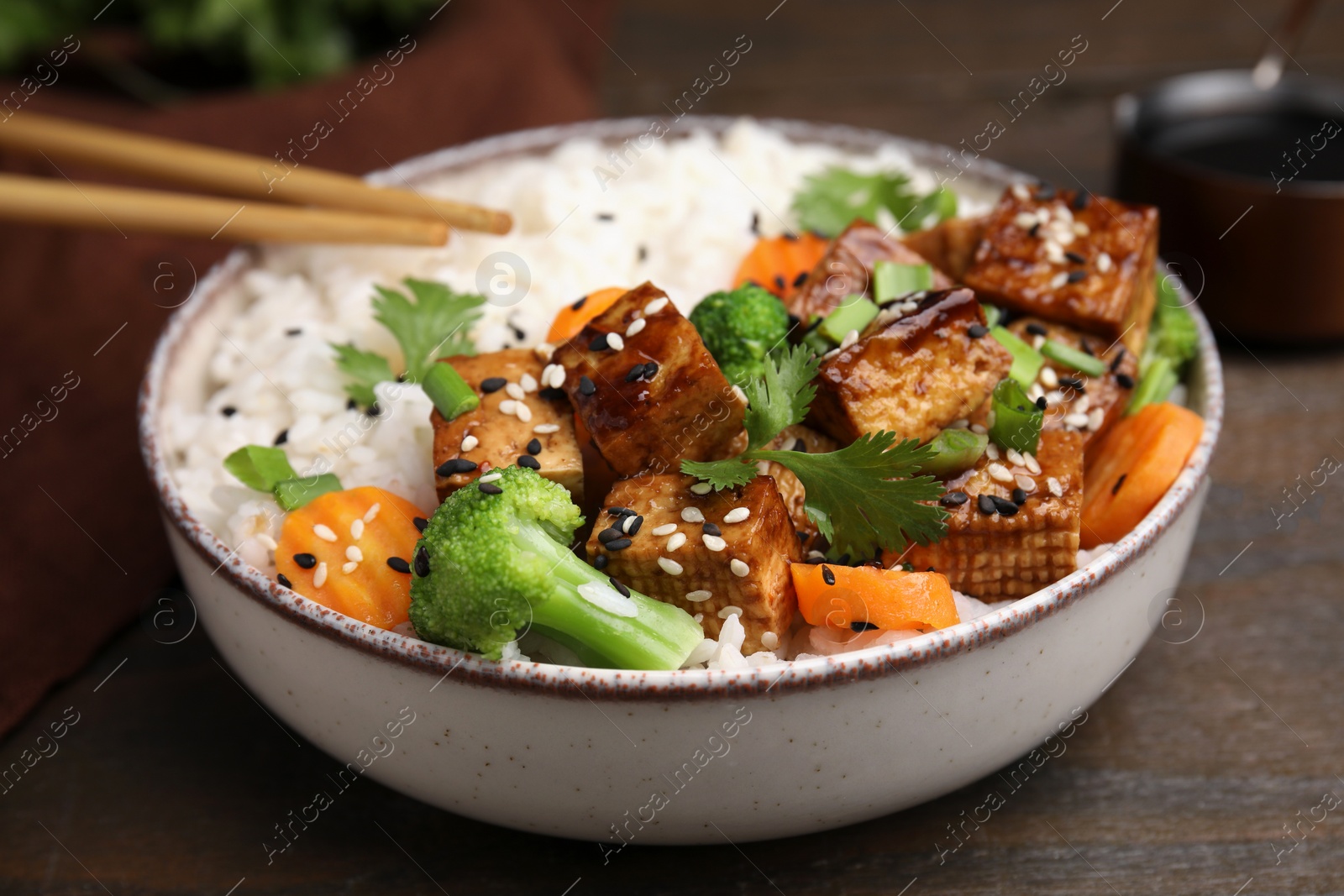 Photo of Bowl of rice with fried tofu, broccoli and carrots on wooden table, closeup