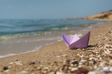 Photo of Paper boat on sandy beach near sea, space for text