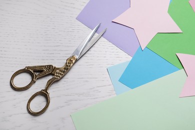 Pair of scissors with colorful paper sheets on white wooden table, flat lay