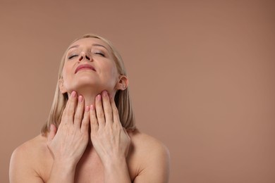 Beautiful woman touching her neck on beige background, space for text