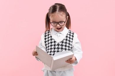 Photo of Cute little girl in glasses reading book on pink background