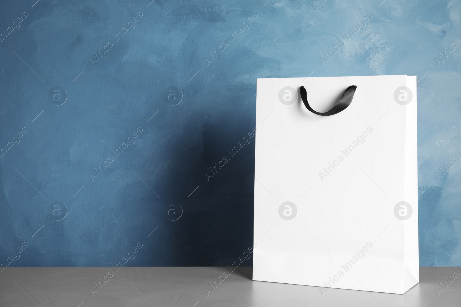 Photo of Paper shopping bag on table against color background. Mock up for design