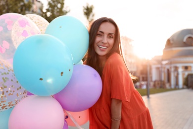 Photo of Cheerful young woman with color balloons outdoors on sunny day