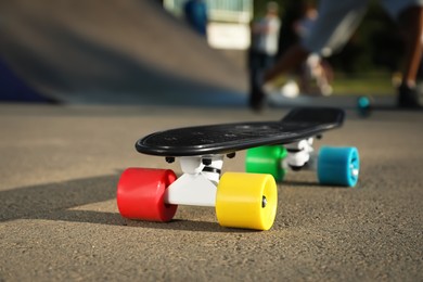 Modern black skateboard with colorful wheels on asphalt road outdoors, closeup