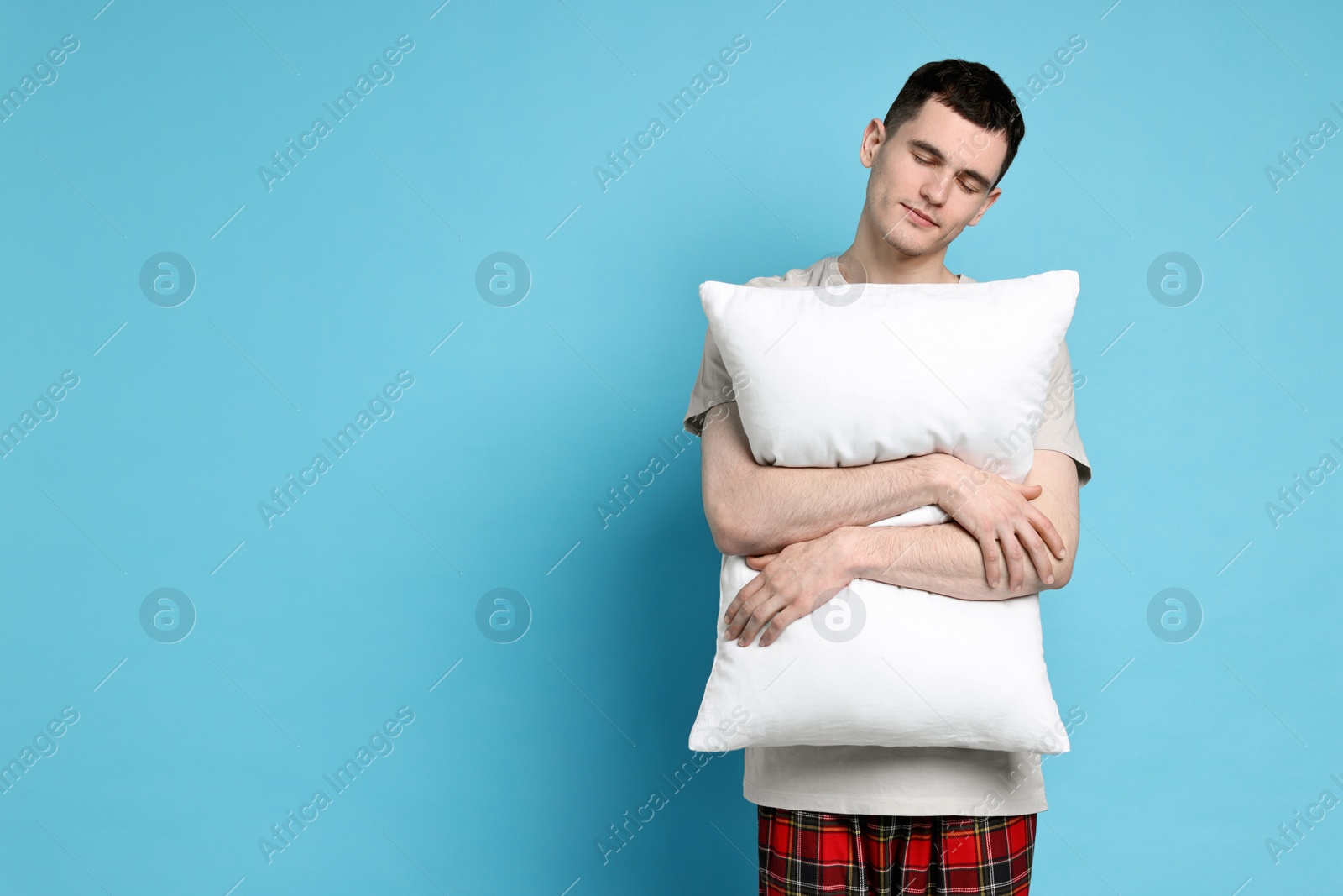 Photo of Man in pyjama holding pillow on light blue background, space for text