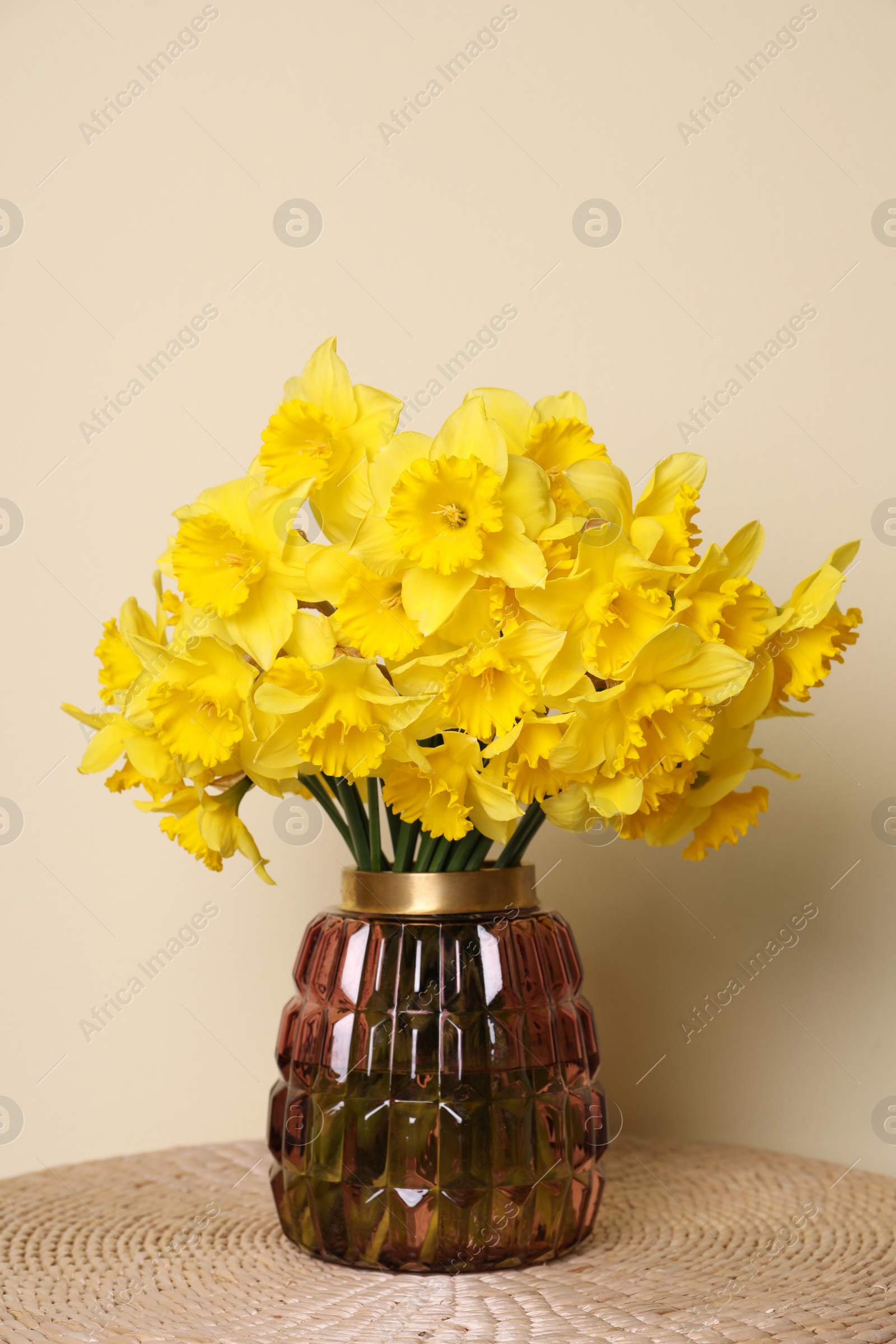 Photo of Beautiful daffodils in vase on wicker table near light wall