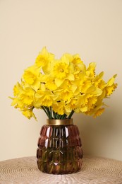 Beautiful daffodils in vase on wicker table near light wall