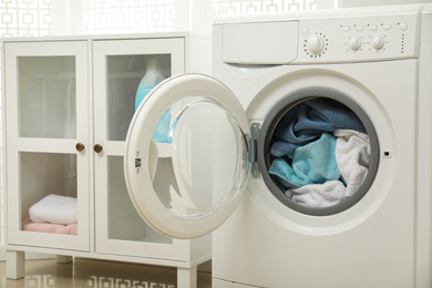 Photo of Modern washing machine with towels in bathroom