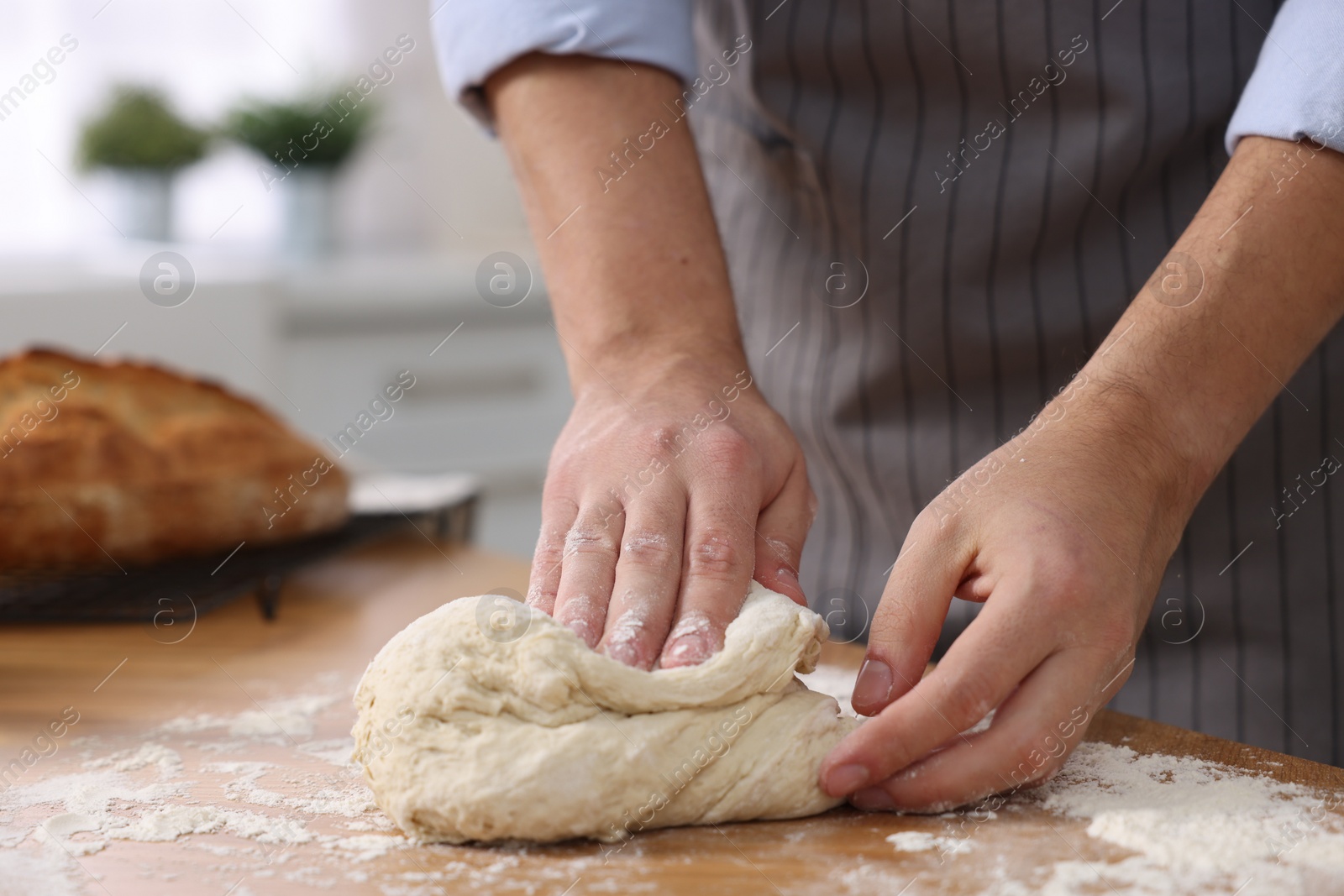 Photo of Making bread. Man kneading dough at wooden table in kitchen, closeup