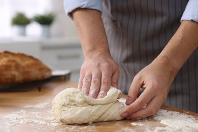 Photo of Making bread. Man kneading dough at wooden table in kitchen, closeup