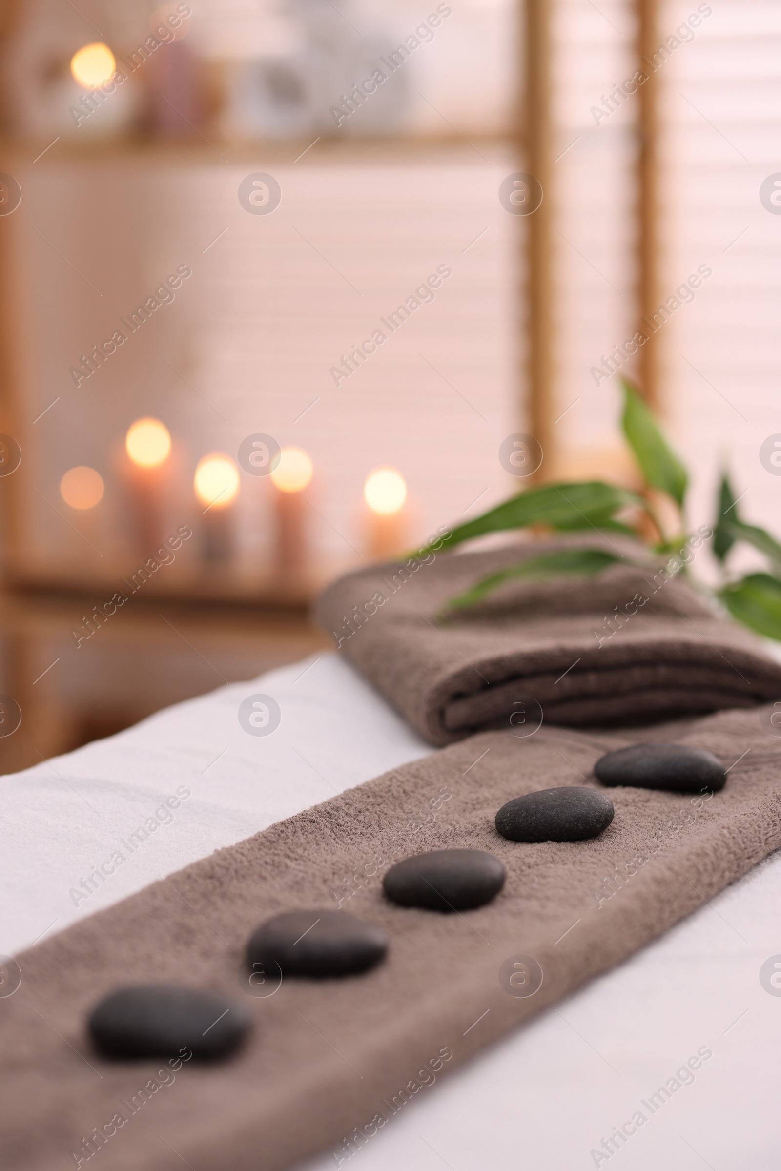 Photo of Towel with arranged spa stones on massage table in recreational center, closeup