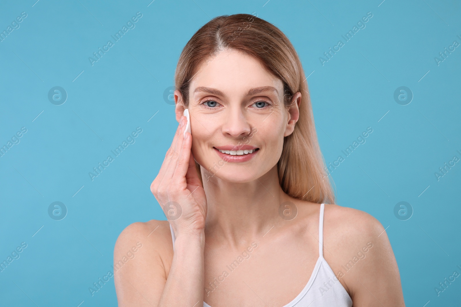 Photo of Beautiful woman removing makeup with cotton pad on light blue background