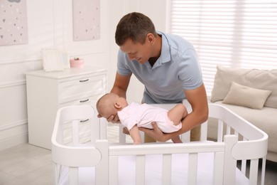 Happy father with his cute sleeping baby near crib at home