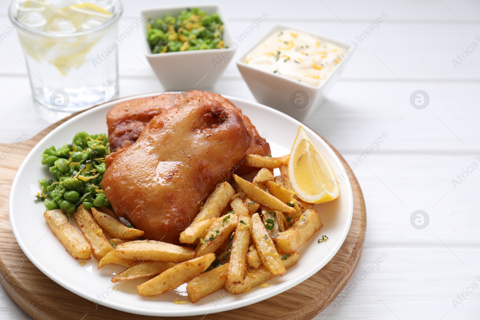 Photo of Tasty fish, chips, sauce, peas and lemon on white wooden table, closeup