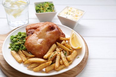 Tasty fish, chips, sauce, peas and lemon on white wooden table, closeup