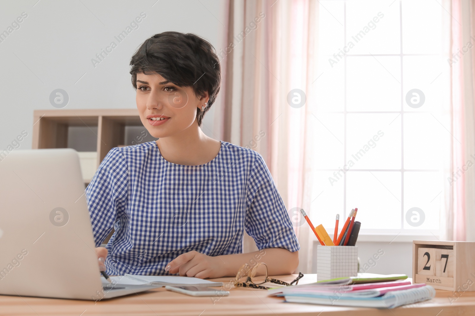 Photo of Young woman working with laptop at desk. Home office