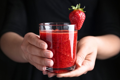 Photo of Woman holding tasty strawberry smoothie on black background, closeup