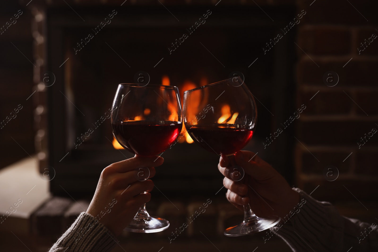 Photo of Couple with glasses of red wine near burning fireplace, closeup