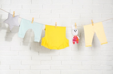 Baby clothes hanging on washing line near white brick wall