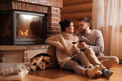 Happy couple with wine near fireplace indoors. Winter vacation