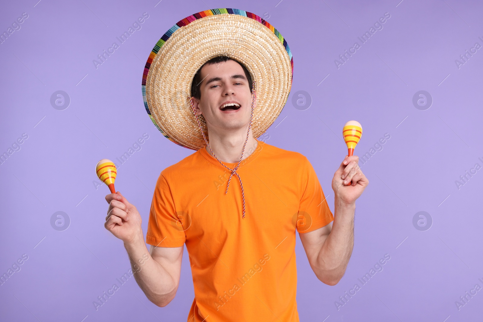 Photo of Young man in Mexican sombrero hat with maracas on violet background