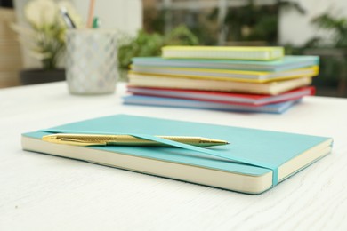 Photo of Turquoise planner and pen on white wooden table indoors, closeup