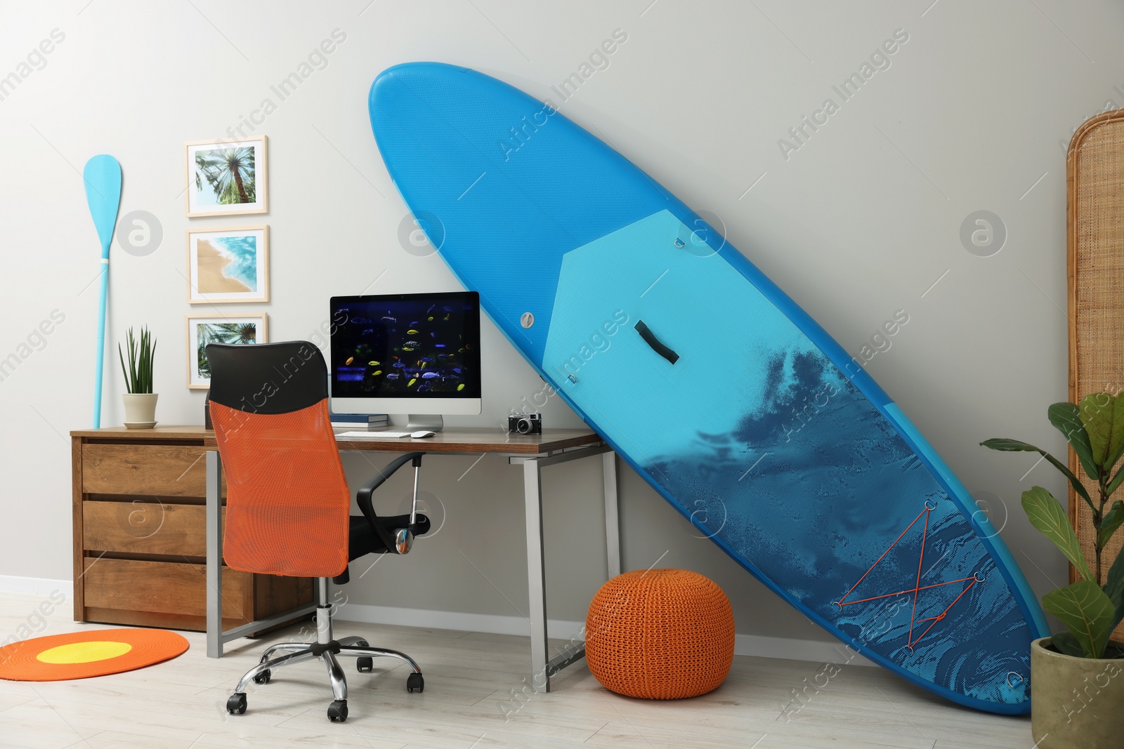 Photo of Stylish workplace with modern computer and SUP board near light wall in room. Interior design