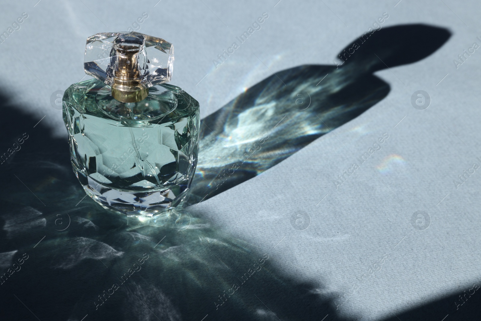 Photo of Luxury women's perfume. Sunlit glass bottle on grey background. Space for text