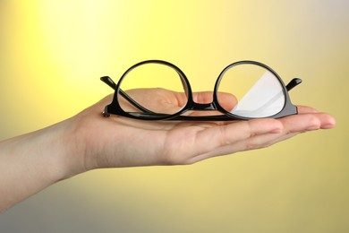 Woman holding glasses with black frame on color background, closeup