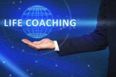 Life coaching concept. Businessman holding virtual globe on blue background, closeup