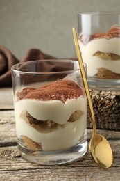 Photo of Delicious tiramisu in glasses and spoon on wooden table