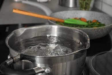 Pot with boiling water on electric stove in kitchen, closeup