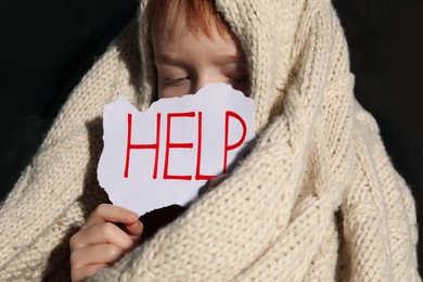 Scared little boy wrapped in blanket holding piece of paper with word Help, closeup. Domestic violence concept