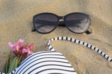 Beautiful sunglasses, swimsuit and tropical flower on sand, closeup