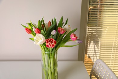 Photo of Beautiful bouquet of colorful tulips in glass vase on table at home