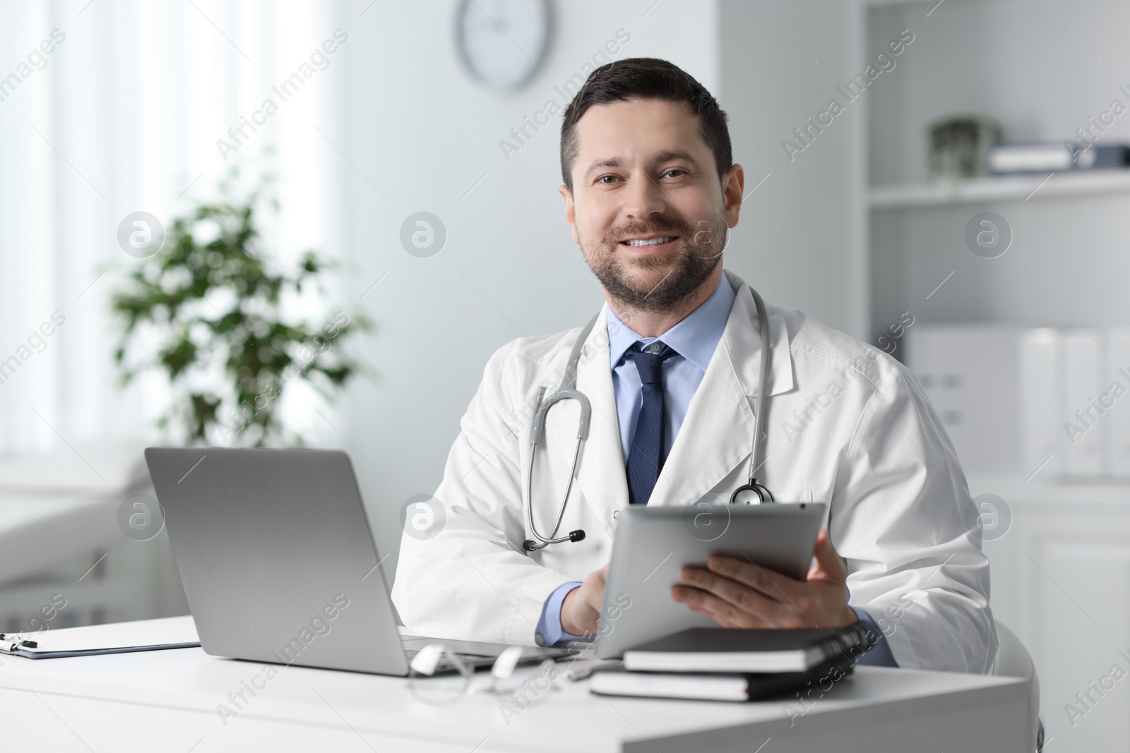 Photo of Smiling doctor with tablet at table in clinic. Online consultation