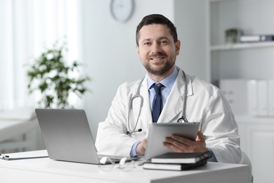 Smiling doctor with tablet at table in clinic. Online consultation