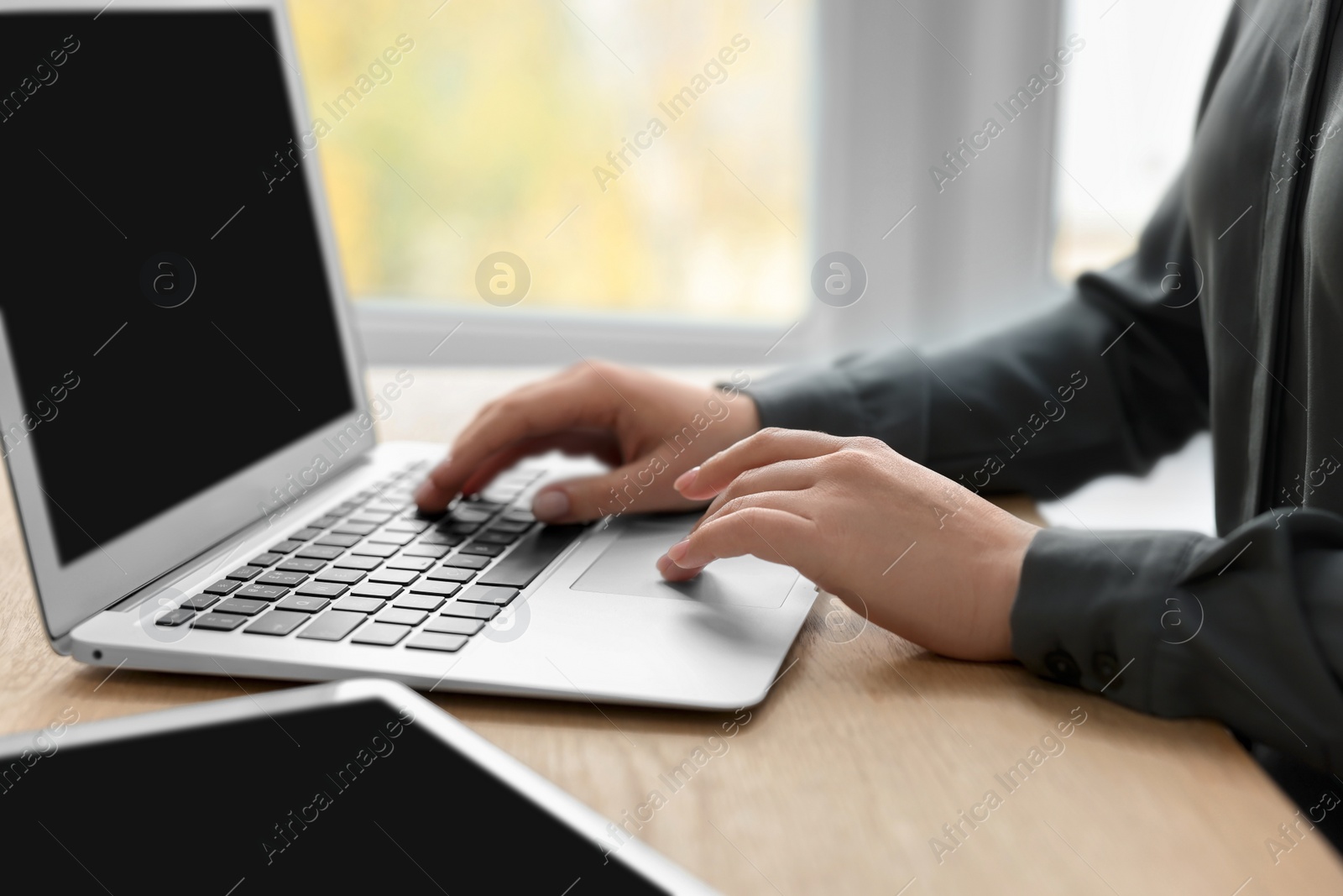 Photo of Woman with tablet working on laptop at wooden table, closeup. Electronic document management