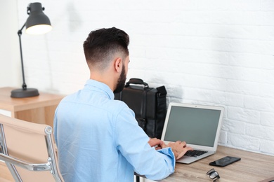 Handsome young man working with laptop at table in home office