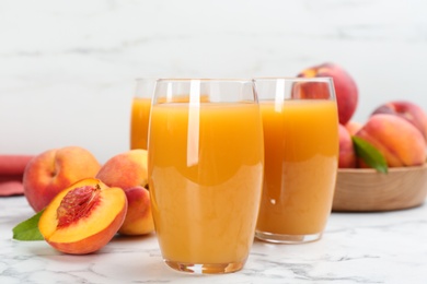 Photo of Natural peach juice and fresh fruits on white marble table, closeup