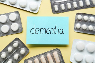 Photo of Paper note with word Dementia and pills on beige background, flat lay