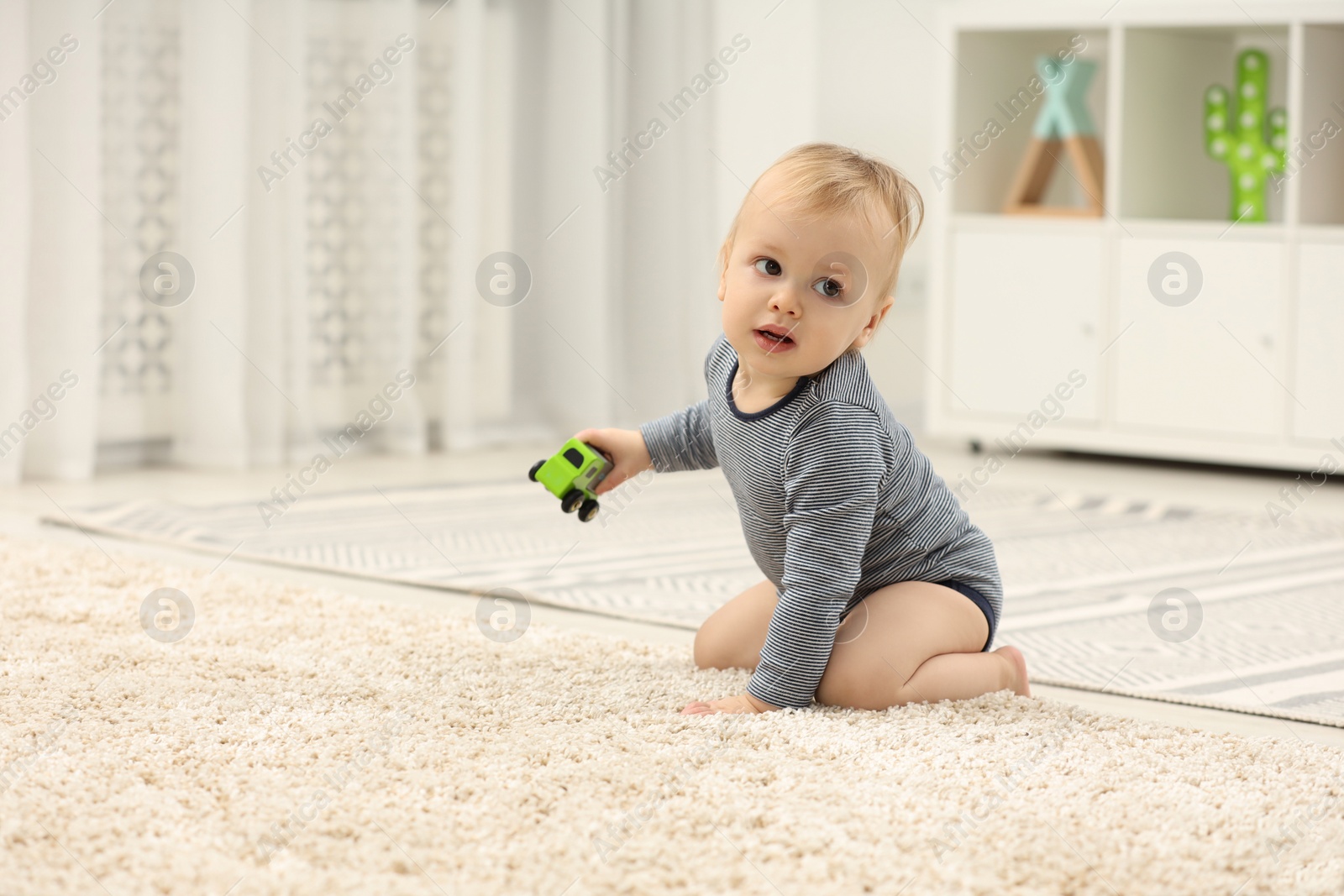 Photo of Children toys. Cute little boy with toy car on rug at home, space for text