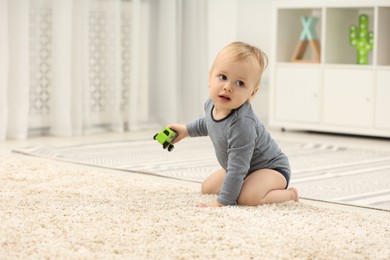 Photo of Children toys. Cute little boy with toy car on rug at home, space for text