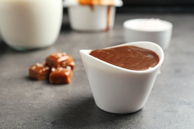 Photo of Bowl with tasty caramel sauce on grey table. Space for text