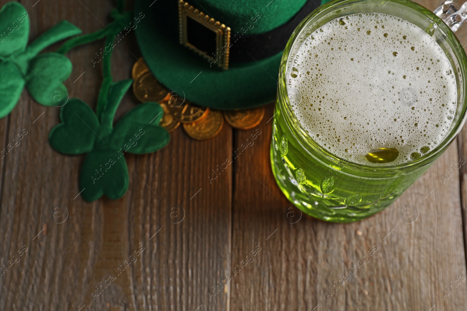 Photo of St. Patrick's day party. Green beer, leprechaun hat, gold and decorative clover leaves on wooden table, above view. Space for text