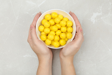 Photo of Woman holding bowl of lemon drops at light table, top view